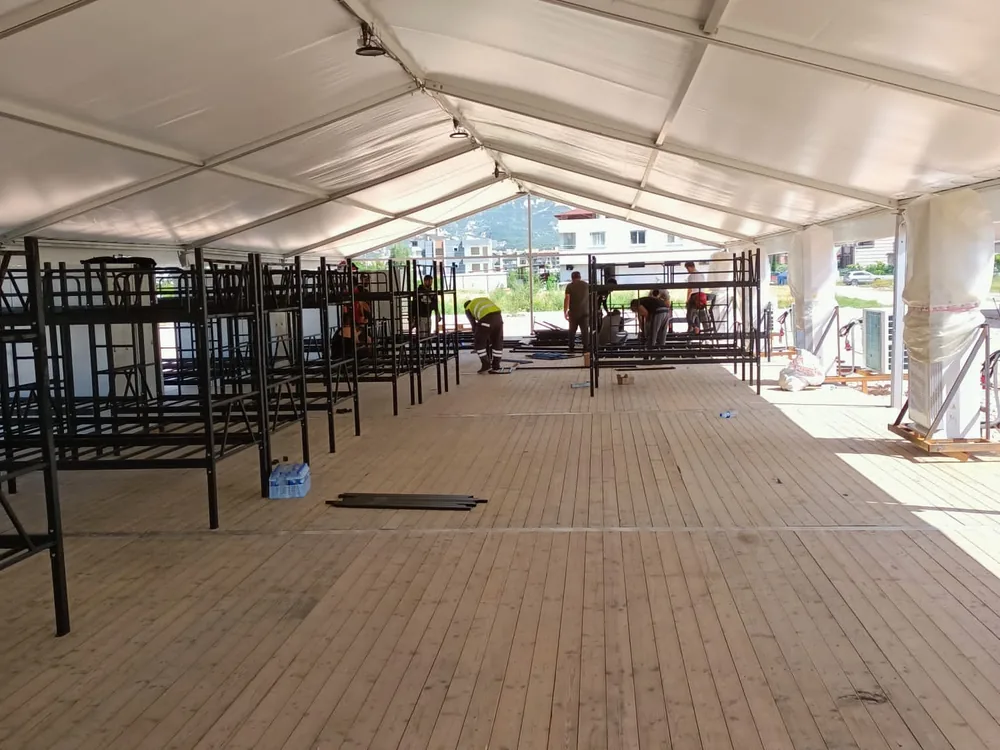Crew assembling bunk bed frames along the length of a tent