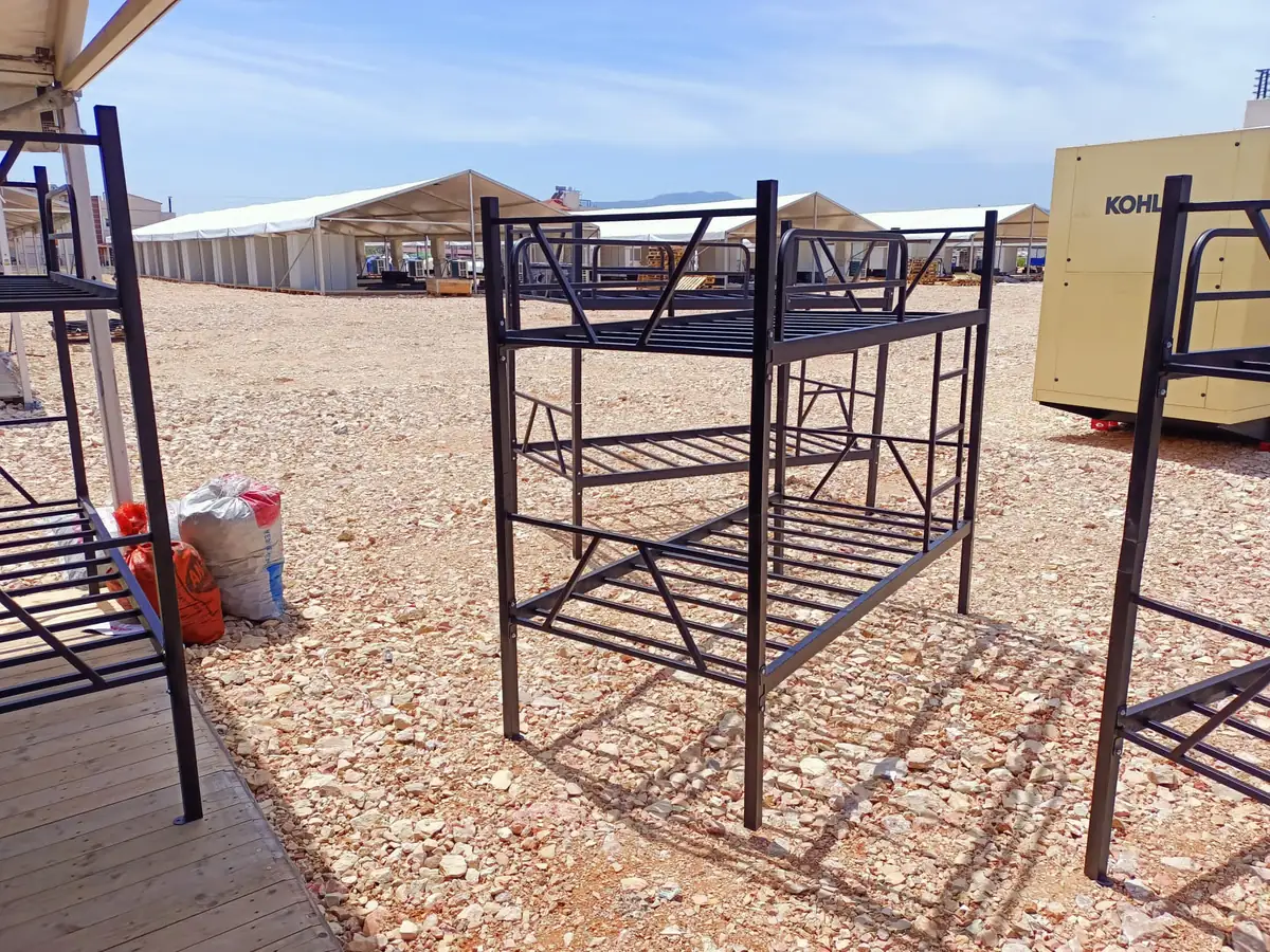 A single assembled black metal bunk bed standing on gravel at the camp