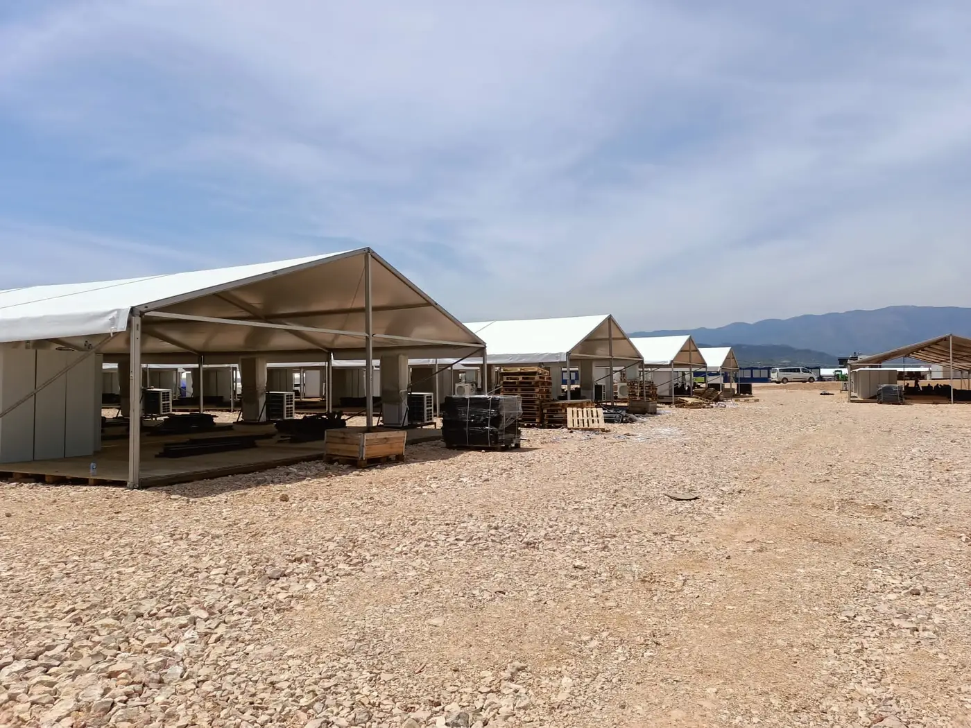 A row of large tents across a gravel site with mountains behind