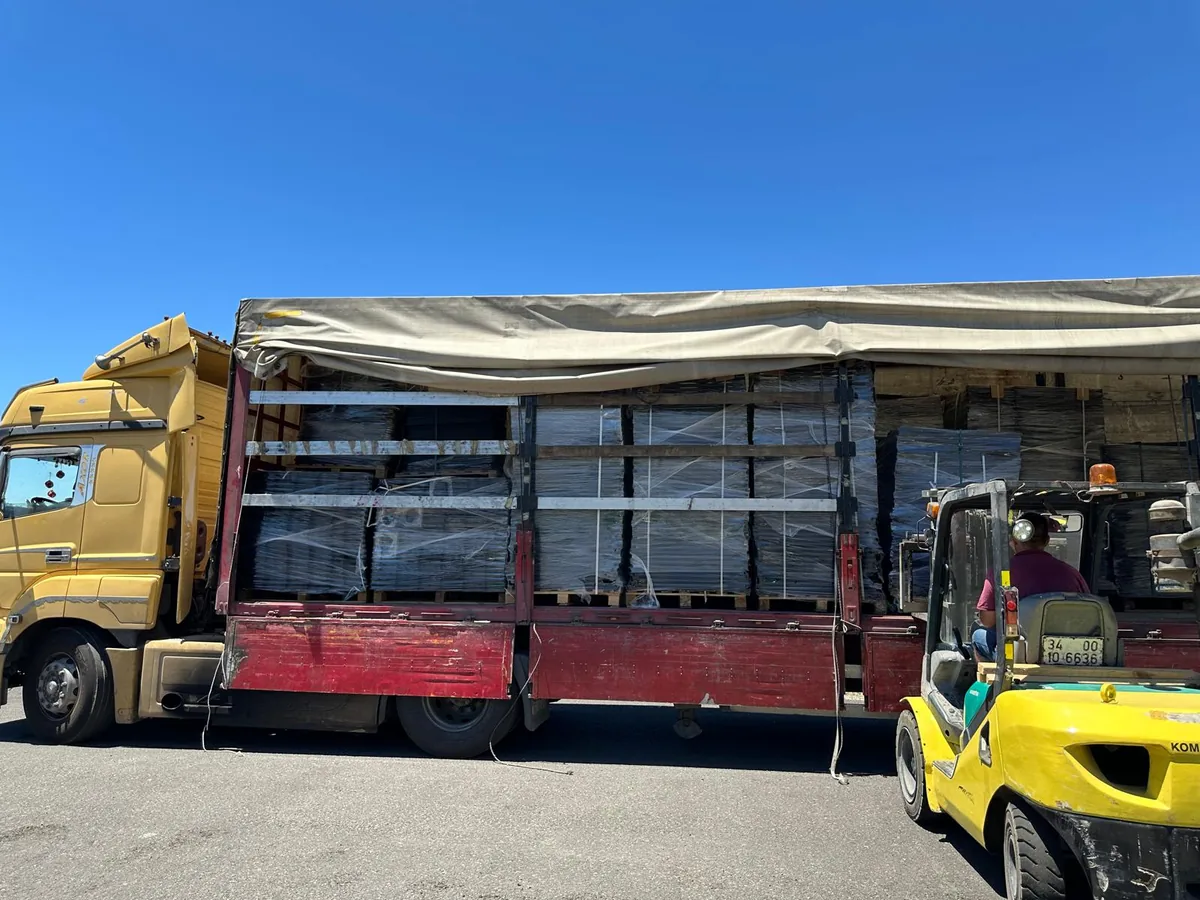 Curtainsider truck loaded with wrapped pallets of flat-packed bunk bed parts, forklift alongside