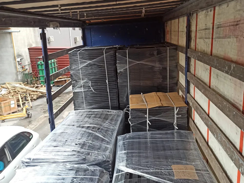 Trailer being loaded in a yard with wrapped bundles of bunk bed frames and mesh bases