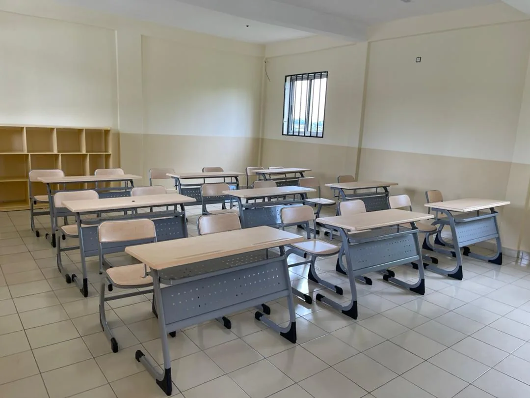 Rows of double school desk and chair sets in a classroom with wall shelving